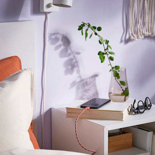 Mesita de noche minimalista con lámpara, planta, libros y cable de carga.