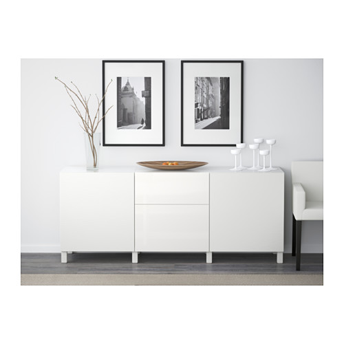 Mueble de almacenaje blanco con cajones y estantes, decorado con elementos de decoración. Las fotos enmarcadas cuelgan por encima.
