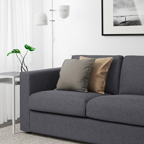 Moderno sofá gris con dos cojines decorativos, colocado contra una pared blanca con un cuadro enmarcado.