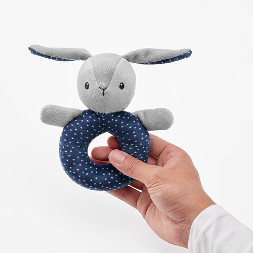 Una mano sostiene un sonajero de conejito de lunares grises y azules, diseñado para que el bebé lo agarre, sacuda y mastique de manera segura.