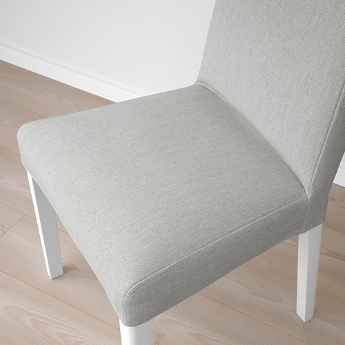 Primer plano de una silla tapizada moderna sobre suelo de madera. La tela de color claro, el diseño elegante y las piernas robustas sugieren comodidad y estilo de alta calidad.