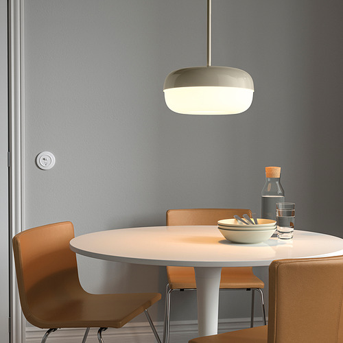 Moderno comedor con mesa redonda, 4 sillas, lámpara cálida, cuencos, vasos y cubiertos junto a la pared gris.