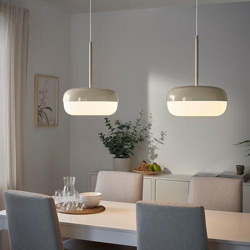 Dos lámparas colgantes BLÅSVERK en color beige cuelgan sobre una mesa de comedor, emitiendo una luz suave en un ambiente de comedor moderno.
