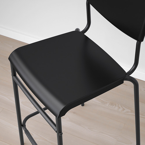 Taburete de bar negro con elegante estructura metálica curvada y asiento acolchado sobre suelo de madera clara.