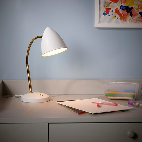 Lámpara de escritorio blanca ISNÅLEN sobre mesa de estudio, cuaderno y bolígrafos iluminados, con colorido arte en la pared.