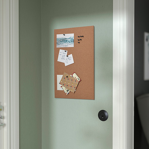 Un tablero de notas de corcho en una pared verde claro contiene fotos, notas y tarjetas con chinchetas negras, exhibidas verticalmente cerca de una puerta.