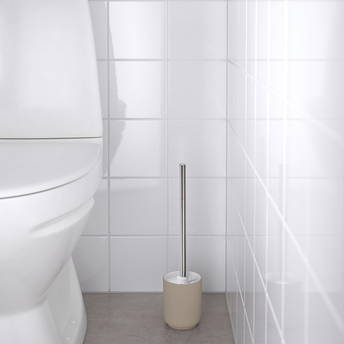 Cuarto de baño con inodoro blanco y soporte de cepillo beige que sostiene cepillo metálico.