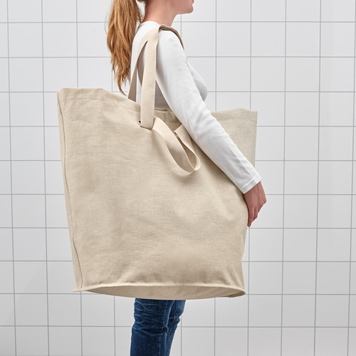 Mujer sosteniendo un gran bolso de lavandería beige con cierre de cordón, diseñado para llevar ropa sucia.