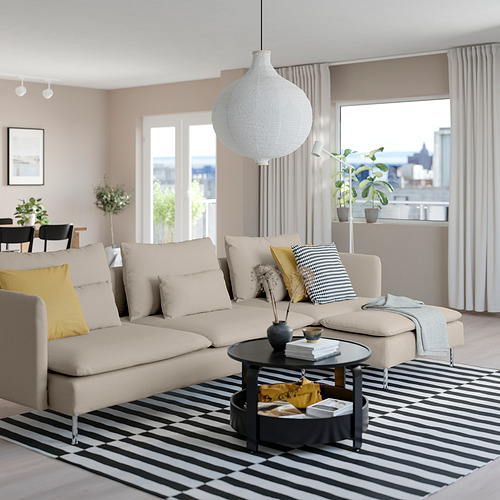 Moderno salón con sofá SÖDERHAMN beige, alfombra de rayas y gran lámpara colgante. Almohadas amarillas en el sofá, ventana grande y mesa de café negra.