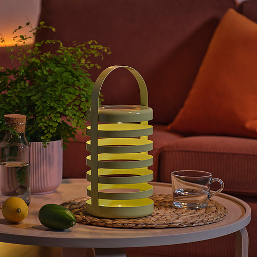 Lámpara moderna sobre la mesa, amarilla brillante, junto a la taza y la fruta.