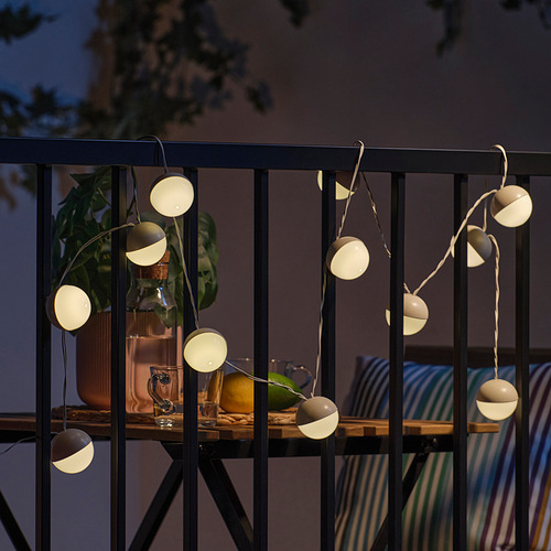 Cadena de orbes resplandecientes que iluminan un balcón; Planta en maceta, tazas y fruta en la mesa.