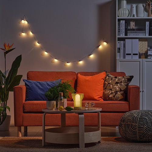 Acogedora sala de estar con sofá naranja, guirnaldas de luces, mesa de centro y estantería.
