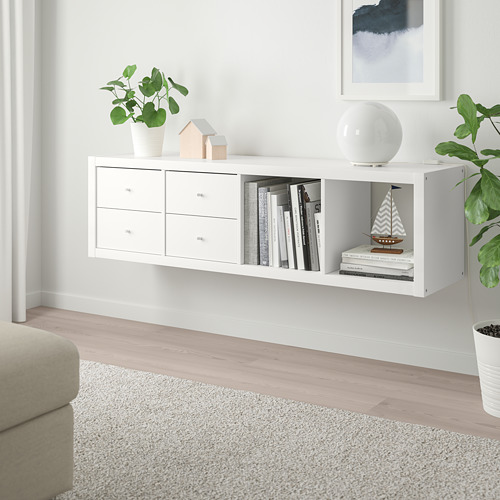 Las estanterías blancas KALLAX de ikea contienen libros, plantas y decoración, estrechas con cajones, entre la decoración de la pared y un sofá.