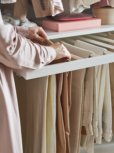 Una persona organiza pantalones beige en una percha blanca de KOMPLEMENT en un armario.