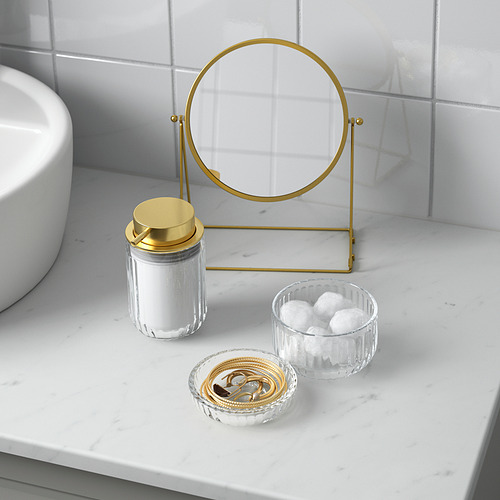 Conjunto de tocador de baño con detalles dorados: espejo circular, frasco de vidrio con tapa y tazones para algodón y joyas.
