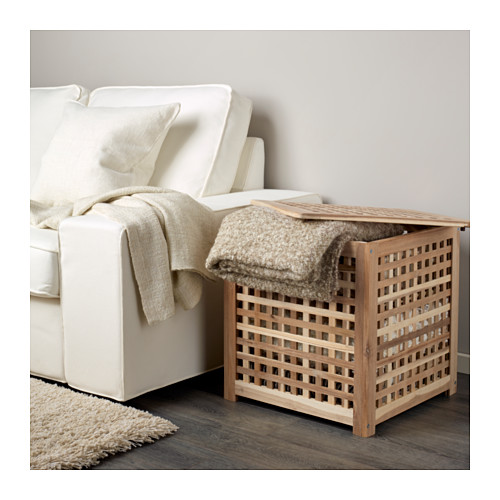 Mesa auxiliar de madera HOL con diseño de celosía junto a sofá blanco, ideal para guardar mantas.