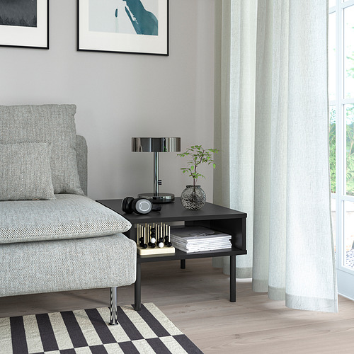 Salón moderno con sofá gris, mesa auxiliar TUNSTA negra, lámpara, planta y ventana con cortinas.