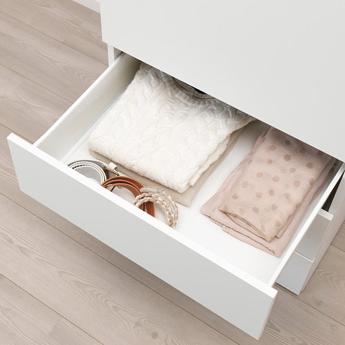 Cajón de armario blanco, toallas cuidadosamente dobladas, cinturones y accesorios guardados en el interior.