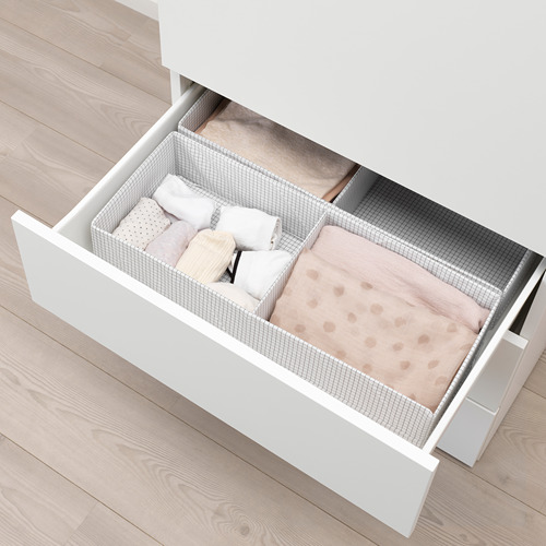 Cajón de armario blanco abierto que muestra una manta y almohadas de color rosa claro cuidadosamente dobladas sobre el suelo de madera.