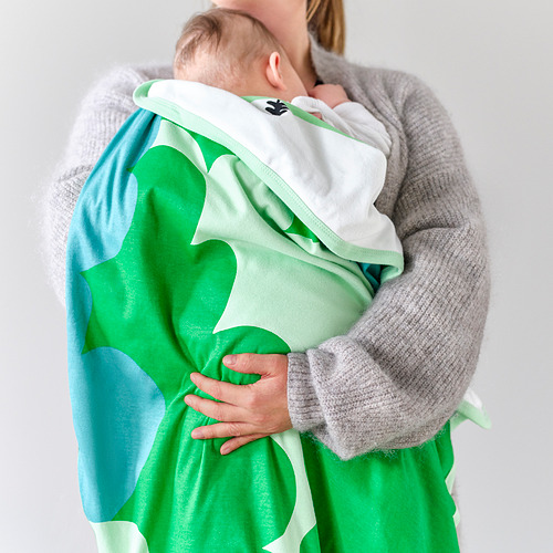 Una persona que sostiene a un bebé en una manta verde y blanca, ideal para la siesta, con un material de algodón suave.