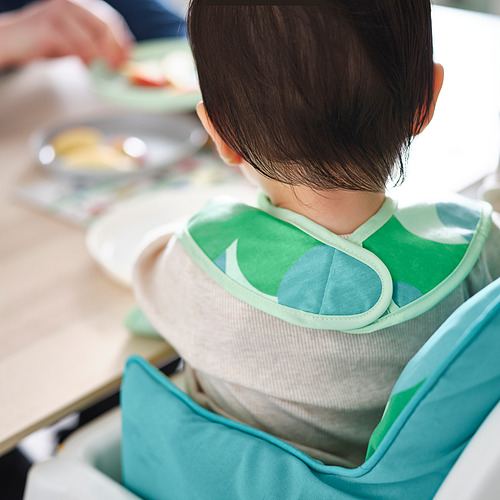 Niño sentado en silla alta con babero verde con bolsillo para recoger la comida, que protege la ropa de derrames.