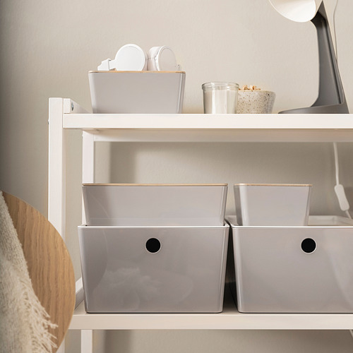 Estanterías blancas con tres cajas KUGGIS grises, organizando pequeños artículos. Las cajas caben perfectamente en los estantes.