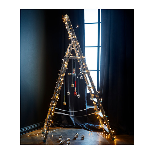 Árbol de navidad triangular único con luces led y adornos contra cortinas oscuras junto a la ventana.