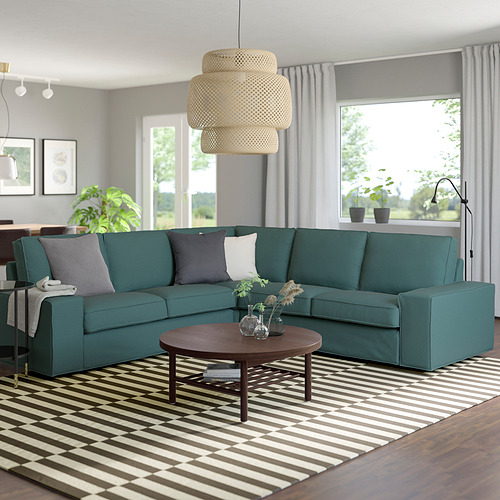 Sofá modular KIVIK verde azulado de diseño moderno, amplio y cómodo, rodeado de alfombra de rayas, mesa de centro de madera y lámpara colgante.