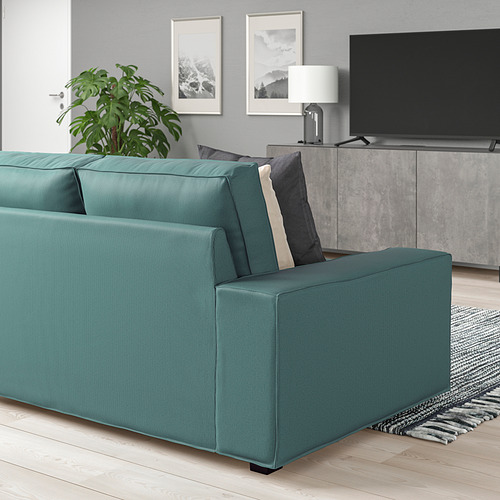 Sofá moderno verde azulado; Grande, acogedor, de perfil bajo. Acentuado por almohadas texturizadas, se sienta debajo de un gran televisor de pantalla plana, decoración gris. 150 caracteres.