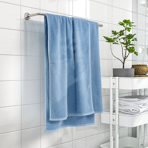 Toalla de algodón azul en la pared del baño junto a estanterías con toallas y plantas.
