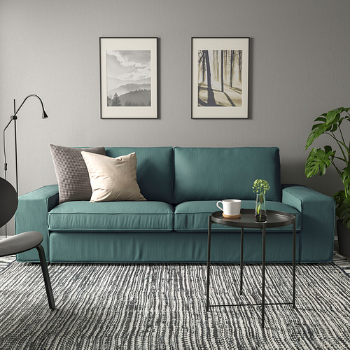Elegante sofá KIVIK en azul-gris, cómodo y moderno salón con fotos de la naturaleza, taza y planta.