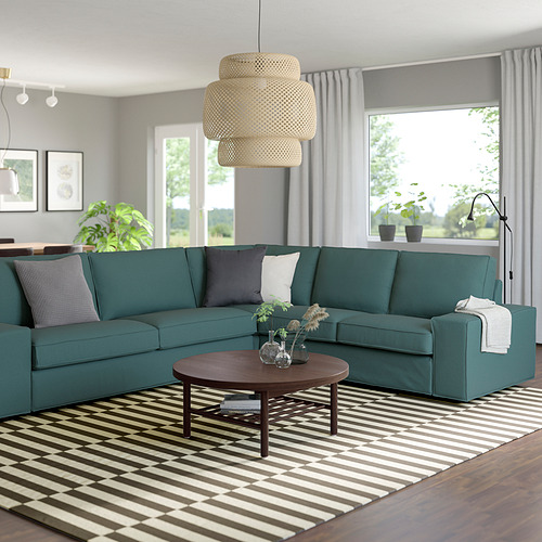 Sofá en forma de L verde azulado en una sala de estar moderna con mesa de centro y alfombra de rayas.