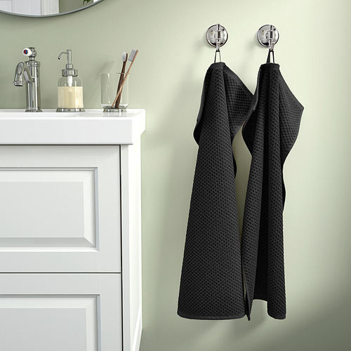 Un baño con una toalla colgante GULVIAL negra, suave y esponjosa, fabricada 100% en algodón, junto a un lavabo blanco con accesorios cromados.