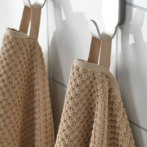 Dos toallas beige cuelgan cuidadosamente en ganchos, mostrando su textura suave y esponjosa y su material duradero.