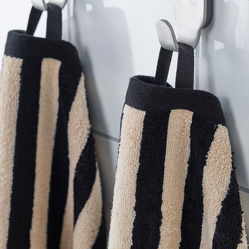 Las toallas de rayas negras y beige cuelgan cuidadosamente de ganchos grises, mostrando su diseño absorbente y decorativo.