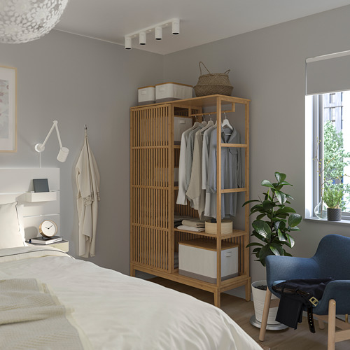 Dormitorio minimalista gris con armario de madera, cama blanca y silla azul. Ropa y plantas decoran la habitación.