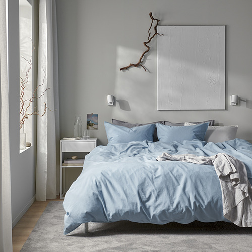 Ropa de cama gris ÄNGSLILJA en cama baja, obras de arte blancas, mesita de noche simple.