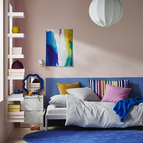 Dormitorio con juego de cama PILTANDVINGE blanco, almohadas de colores, arte de pared, lámpara colgante, estantes blancos y alfombra azul, organizada y luminosa.