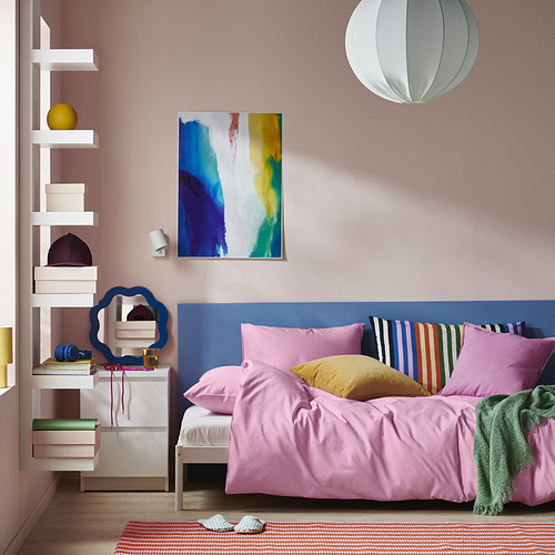 Edredón PILTANDVINGE de color rosa brillante sobre cama azul, con almohadas de colores, contra una pared rosa con arte abstracto.