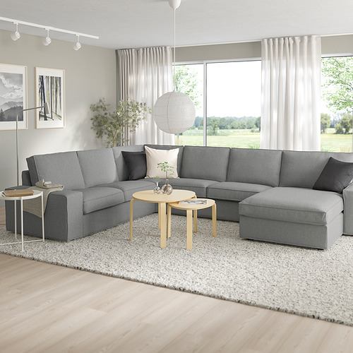 Sala de estar moderna con un gran sofá seccional KIVIK gris, dos mesas auxiliares, alfombra y un gran ventanal con vista a la vegetación.