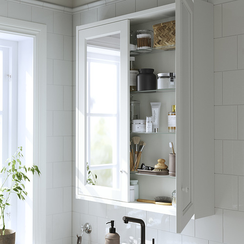 Un mueble de baño blanco con espejo, con paneles biselados, y estantes de vidrio que guardan artículos de tocador y papel higiénico.