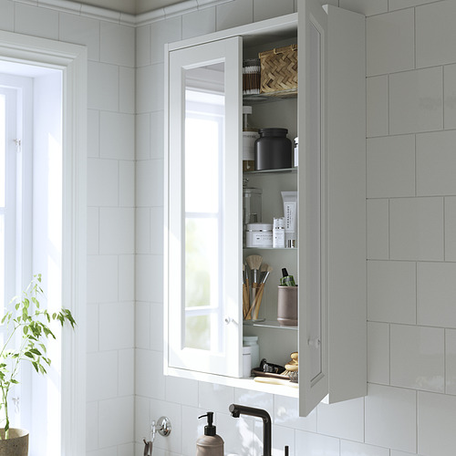 Mueble de baño blanco con puertas de vidrio para guardar artículos de tocador y maquillaje, montado sobre un lavabo con un espejo.