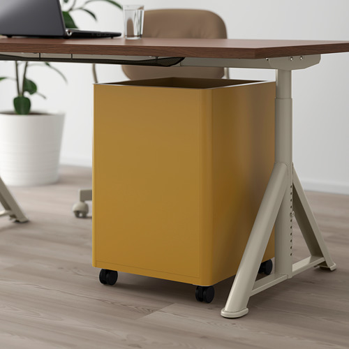 Una cajonera IDÅSEN amarilla con ruedas debajo de un escritorio con amortiguadores integrados para un cierre suave.