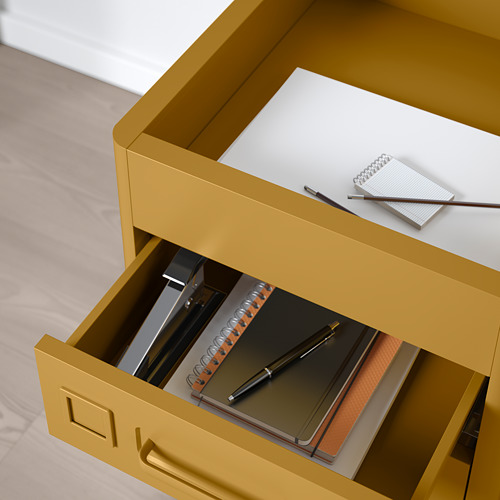 Cajonera de oficina de color amarillo mostaza con compartimentos abiertos. Los elementos mostrados incluyen cuadernos y bolígrafos, mostrando la organización integrada.