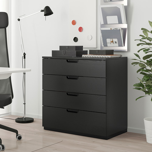 Cofre GALANT ikea: mueble negro de 4 cajones junto al escritorio, silla, lámpara. La parte superior tiene cajas, papeles. Fondo: pizarra, estantería.