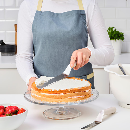 Una persona está glaseando un pastel con una espátula en la encimera de la cocina. Un cuenco de fresas está cerca.