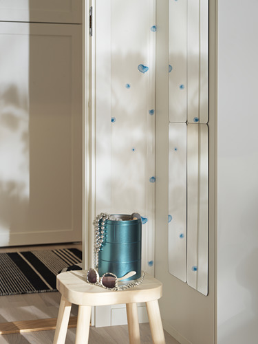 Taburete pequeño blanco con jarrón azul y accesorios. Detrás, un espejo de armario alto con calcomanías azules.