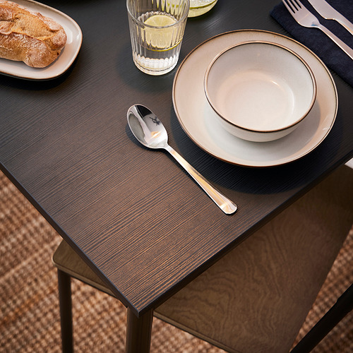 Montaje de la mesa con mesa de arenkín, con tapa de madera oscura y patas de metal, junto con platos ligeros, una cuchara y un vaso de limonada.