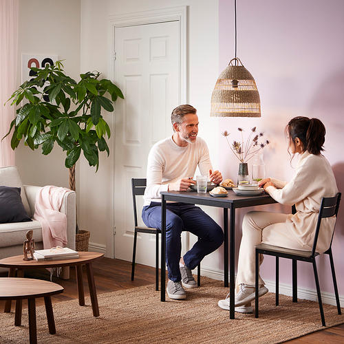 Una pareja disfruta del desayuno en una mesa de comedor de arenberg con patas de metal y una tapa de madera en una acogedora habitación de temática rosa.