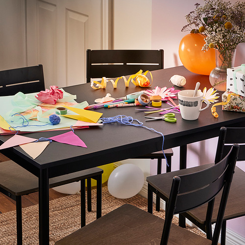 Coloridas manualidades en mesa de arenado con sillas, globo naranja, tijeras, cintas y jarrón.